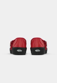 Rde slip-on čevlje Vans z debelimi črnimi podplati in logotipi "Off The Wall" na hrbtni strani, prikazani z zadnjega vidika na beli podlagi.