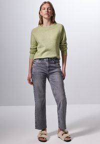 Ljusgrön tröja, grå högmidjade jeans och beige fluffiga tofflor. Tröjan har långa ärmar och rund hals.