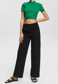 Haut court côtelé vert avec des découpes, associé à un pantalon noir à coupe ample et des sandales noires à enfiler. Design minimaliste, textures lisses.