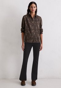 Brązowa koszula zapinana na guziki w kwiatowy wzór, z podwiniętymi rękawami, zestawiona z czarnymi rozszerzanymi spodniami i brązowymi butami. Gładka faktura materiału, dopasowany krój.