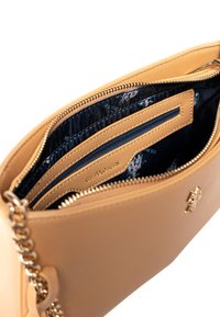 Borsa a tracolla in pelle color cuoio con chiusura a zip, dotata di scomparti per carte interne, una fodera a motivo scuro e dettagli in metallo dorato.
