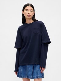 Námornícky modré oversized tričko s krátkymi rukávmi a malou náprsní kapsou, nosené s džínsovou sukňou s výraznými švami a roztrhnutým lemom.