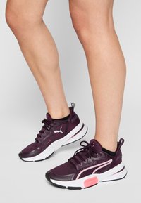 Zapatillas deportivas moradas hechas de malla transpirable, con detalles en negro, suelas blancas y detalles rosas en el talón y el logo.
