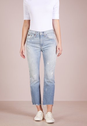 Lichtblauwe, versleten denim jeans met verfspetters, rechte pijpen, rauwe zooms en een hoge taille, gecombineerd met witte sneakers.