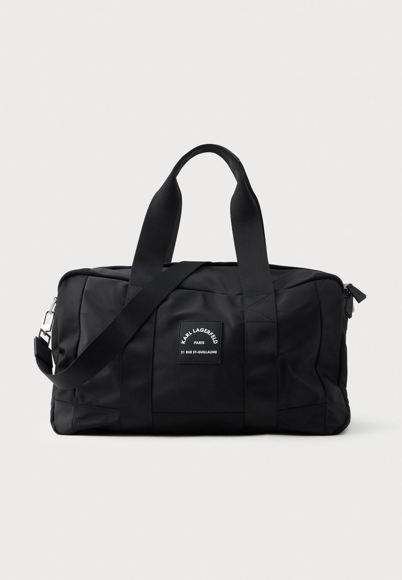 Fekete, nylon anyagú sporttáska, kettős felső fogantyúval, levehető vállpánttal és téglalap alakú testtel, logóval ellátott folttal.