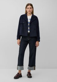 Marineblauer gekürzter Peacoat mit doppelt geknöpftem Vorderteil, breiten Revers und großen Knöpfen, kombiniert mit dunklen Jeans und glänzenden burgunderfarbenen Slippern.