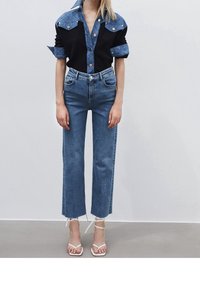 Jeansskjorta med mörk kropp och ljusblå vadderade axlar; matchad med högmidjade raka jeans och vita sandaler med remmar.