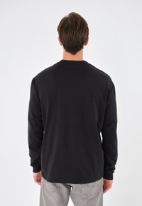 Svart långärmad t-shirt med rund halsringning, tillverkad av bomull. Baksidan har en jämn textur och en rak skärning utan synliga logotyper.