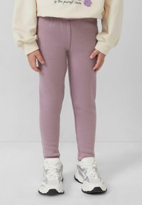 Fioletowe legginsy wykonane z elastycznego materiału, charakteryzujące się gładką teksturą i dopasowanym krojem, w połączeniu z białymi i srebrnymi butami sportowymi.