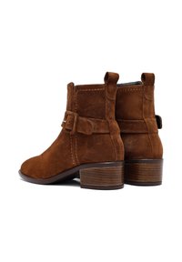 Stivaletti alla caviglia in suede marrone con punta arrotondata, cuciture decorative, cinturino alla caviglia con fibbia e tacco in legno impilato.