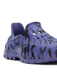 Chaussure violette à enfiler avec motif abstrait noir, trous de ventilation et semelle texturée, vue en angle sur fond blanc.