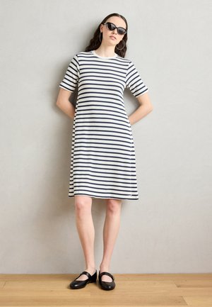 Gestreiftes kurzärmliges Kleid in Creme und Marineblau, knielang, aus geripptem Stoff. Kombiniert mit schwarzen Mary Jane Schuhen und Sonnenbrille.