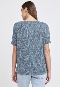 Blommönstrad turkosskjorta med kort ärm och avslappnad passform. Har en rund halsringning och mjukt tyg. Lätta inslag av rosa och vitt i mönstret.