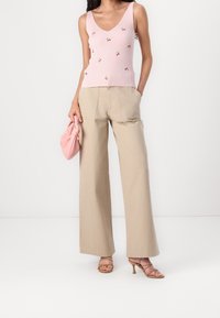 Różowa, prążkowana koszulka na ramiączkach z haftowanymi detalami w kształcie wiśni, w zestawie z beżowymi spodniami o szerokich nogawkach i różowym kopertówką. Brązowe sandały na obcasie.