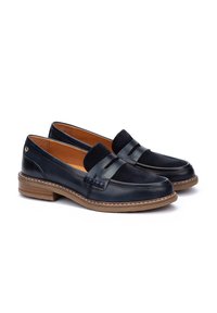 Mocasines de cuero negro con detalles en ante, puntera redonda y suela baja marrón. Las costuras detalladas añaden textura e interés visual.