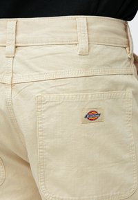 Μπεζ παντελόνι με εμφανείς ραφές και πίσω τσέπη που φέρει ένα μικρό ορθογώνιο λογότυπο Dickies.