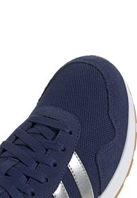 Baskets bleu marine présentant un dessus en maille texturée, des accents en suede lisse, une bande métallique argentée et une semelle en caoutchouc beige.