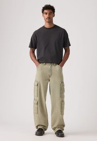 Μαύρο βαμβακερό μπλουζάκι σε συνδυασμό με ανοιχτόχρωμο ελιάς παντελόνι cargo με πολλές τσέπες και άνετη εφαρμογή, ολοκληρωμένο με μαύρα παπούτσια.