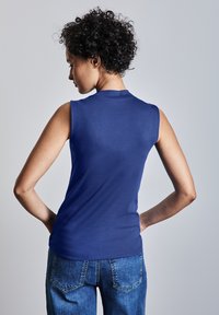 Ärmlös, blå topp i ett mjukt tyg, med en rundad halsringning och en figursydd form, bärs tillsammans med ljusblå jeans.