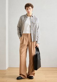 Camisa de cuadros clara en azul y amarillo, camiseta blanca, pantalones beige ajustados, bolso negro y zapatos negros gruesos.
