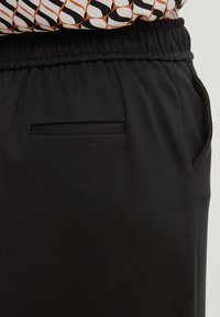 Black jogger pants with a smooth texture, featuring an elastic waistband and a small, horizontal pocket on the side.