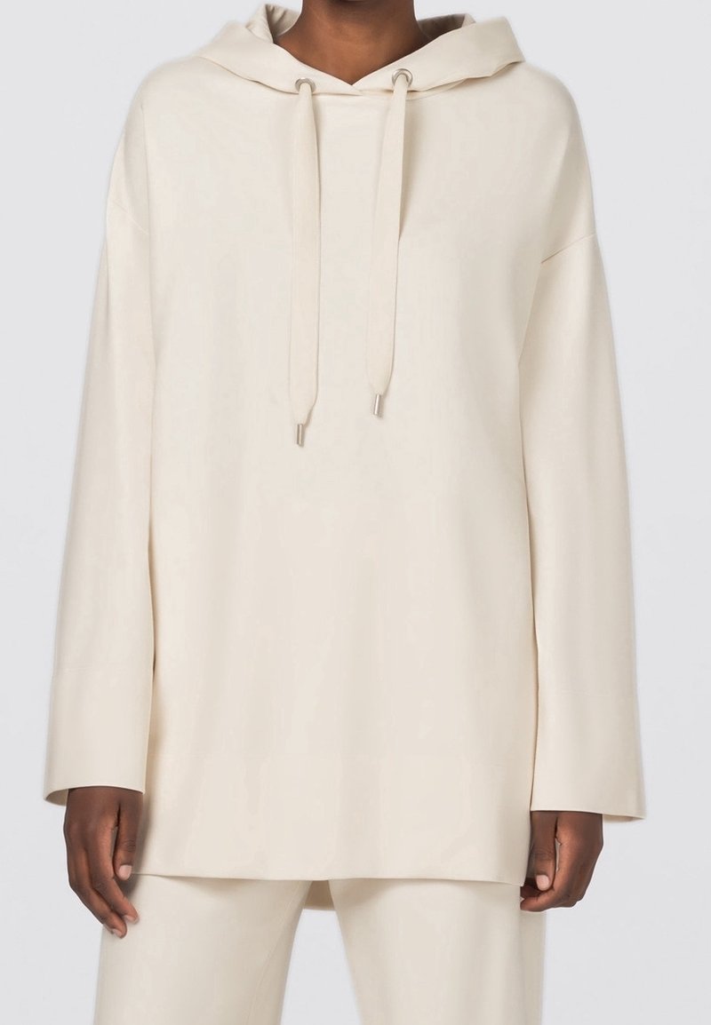 Sudadera beige de gran tamaño con cordón, mangas largas y textura suave. Diseño sencillo, con detalles mínimos y corte relajado.