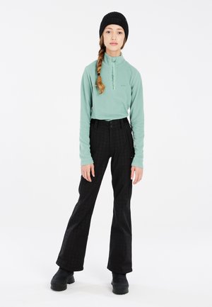 Mintgroene fleece half-zip top, zwarte geklede wijde broek, en een zwarte gebreide beanie, gecombineerd met zwarte schoeisel, tegen een witte achtergrond.