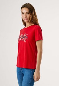 T-shirt en coton rouge à manches courtes et col rond. Présente un imprimé floral en blanc et bleu sur la poitrine.
