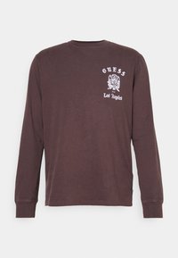 Camicia a maniche lunghe marrone in cotone, con un logo grafico bianco sul lato sinistro del petto. Collo a giro e polsini aderenti.