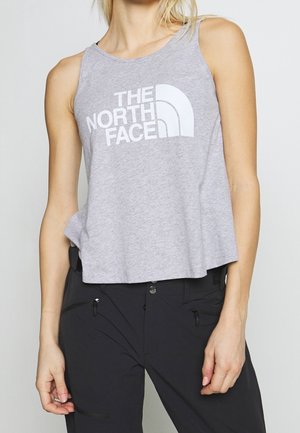Vrouw draagt een grijze mouwloze top met "The North Face"-logo en zwarte broek met ritszakken.