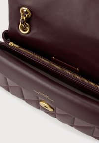 Bordo kožna torba za rame s kvadratnom teksturom, zlatnim detaljima, džepom na zatvarač i utisnutim logotipom koji glasi "The Tabby Bag Genuine Full Grain Leather."