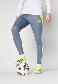 Gray athletic pants with white stripes, featuring a neon yellow accent. Paired with bright green soccer cleats on a patterned soccer ball.