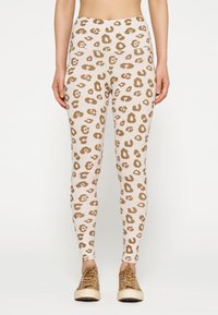 Leggings beige chiaro con un motivo a leopardo marrone, dotati di vita alta e vestibilità aderente, abbinati a sneakers marroni.