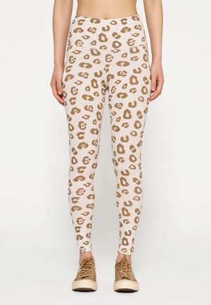 Leggings beige chiaro con un motivo a leopardo marrone, dotati di vita alta e vestibilità aderente, abbinati a sneakers marroni.