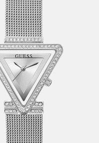 Sølv trekantet ur med meshrem, krystal accenter rundt bezelen og en minimalistisk skive med sorte timemarkører og visere.