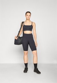 Sostenedor deportivo negro y pantalones cortos de ciclismo de cintura alta hechos de material elástico. Acompañado de un bolso de deporte negro y zapatillas negras.