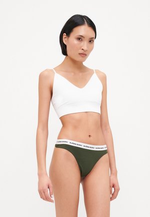 White v-neck bralette and olive green thong with a white waistband featuring the brand name. Soft fabric, seamless design, minimal details.
