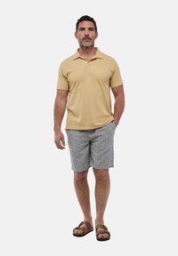 Polo shirt beige clair, short rayé gris et sandales brunes. Le polo a un col et des manches courtes. Tenue décontractée.