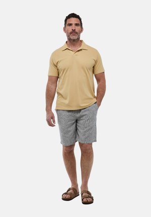 Polo shirt beige clair, short rayé gris et sandales brunes. Le polo a un col et des manches courtes. Tenue décontractée.