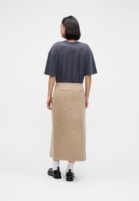 Přehnaně velké šedé tričko ve spojení s béžovou maxi sukní z vlny. Sukně má dvě zadní kapsy a hladkou texturu. Černá obuv doplňuje celkový vzhled.