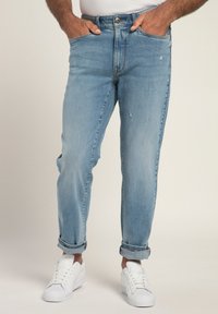 Jeans de mezclilla azul claro con un corte relajado, que presentan detalles desgastados y dobladillos enrollados, combinados con zapatillas blancas.