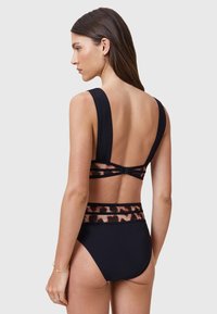 Set bikini nero a due pezzi con spalline larghe. La parte superiore presenta una fascia con stampa animale a contrasto. Parte inferiore a vita alta in tessuto nero solido.