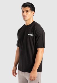 Sort bomulds T-shirt med rund hals og korte ærmer, med hvid "SMILODOX" tekst på venstre brystområde. Simpelt design.
