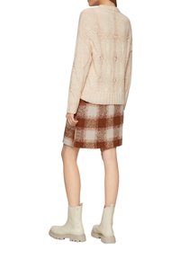 Beige gestrickter Pullover mit strukturiertem Muster, kombiniert mit einem karierten Rock in Braun und Creme. Das Model trägt hellbeige Knöchelstiefel mit dicken Sohlen.