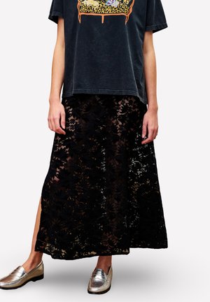 Jupe midi en dentelle florale noire avec fente latérale portée avec un t-shirt graphique noir délavé et des mocassins métalliques argentés sur une personne.