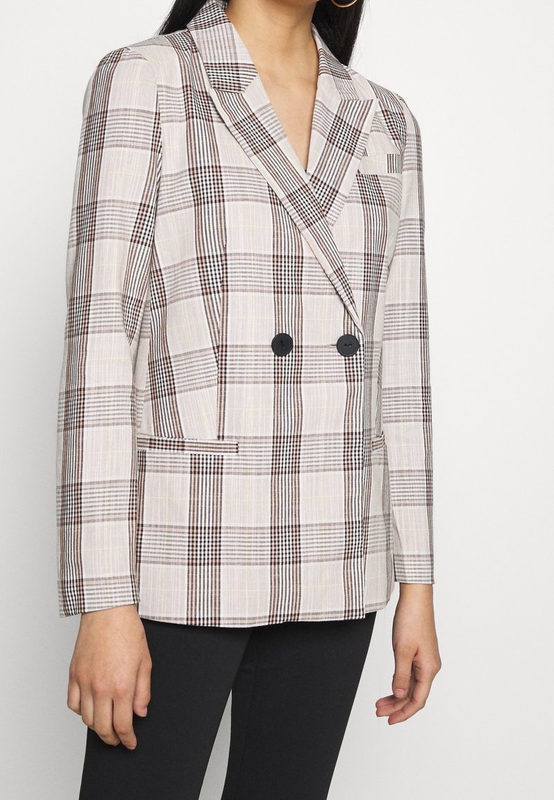 Blazer doppiopetto in un tessuto beige chiaro con motivo a quadri marroni, bottoni neri e colletto a scialle; include tasche laterali.