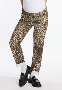 Pantalons à imprimé léopard marron et beige, avec une coupe décontractée, des ourlets retroussés et une fermeture à bouton sur le devant, associés à des mocassins noirs.