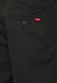 Černé kalhoty vyrobené z odolné tkaniny, s přední kapsou, zapínáním na knoflík a červenou nášivkou Levi's na zadní straně.