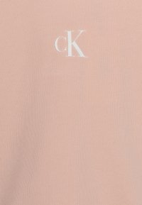 Light pink cotton t-shirt featuring a white "cK" logo. Material has a smooth texture and a classic crew neckline design.