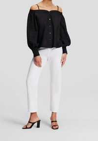 Svart avskuren blus med knäppning fram, puffiga genomskinliga ärmar och broderie anglaise-detalj, kombinerad med vita raka jeans och svarta klackskor.